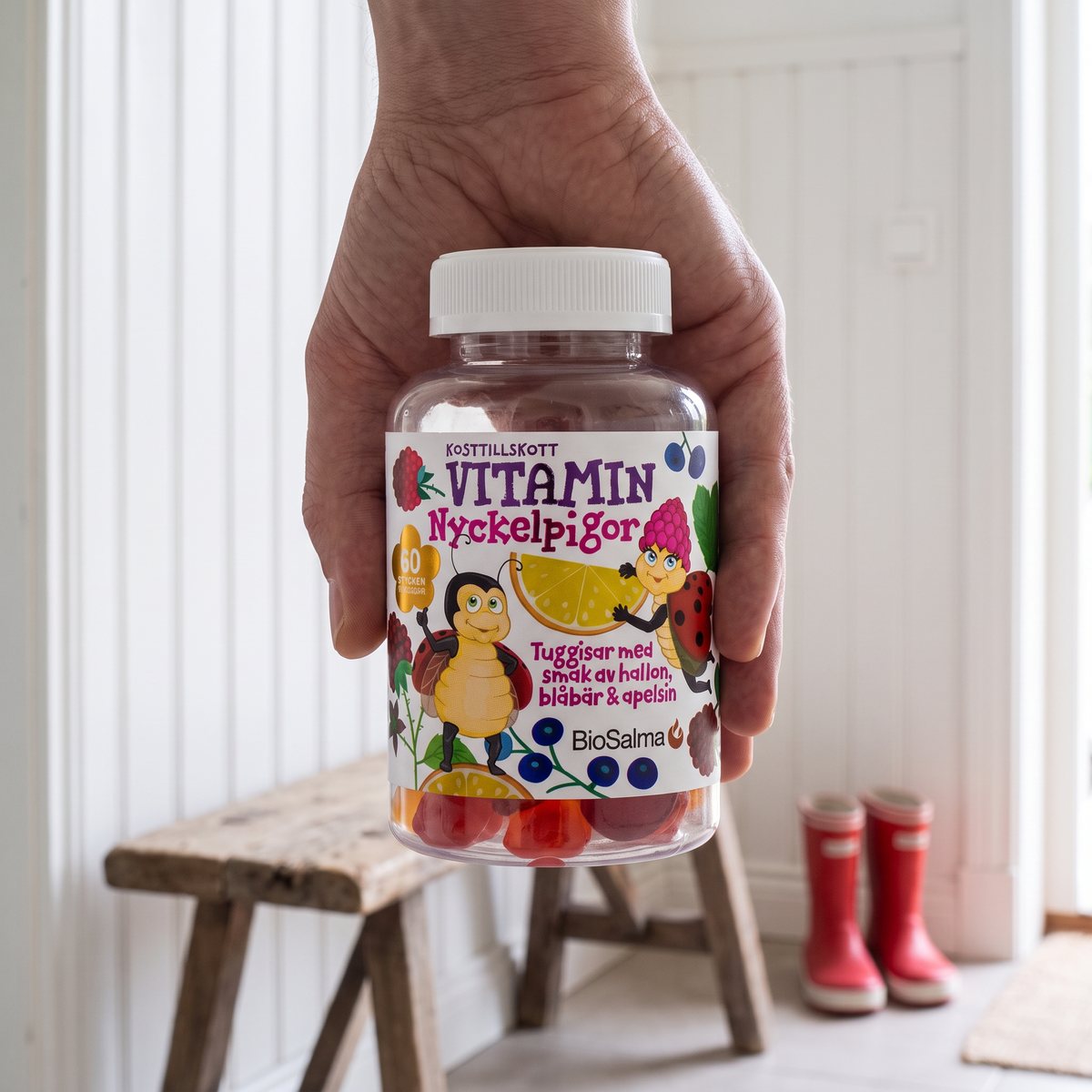 Hand håller burken BioSalma Multivitamin Nyckelpiga i en svensk hall