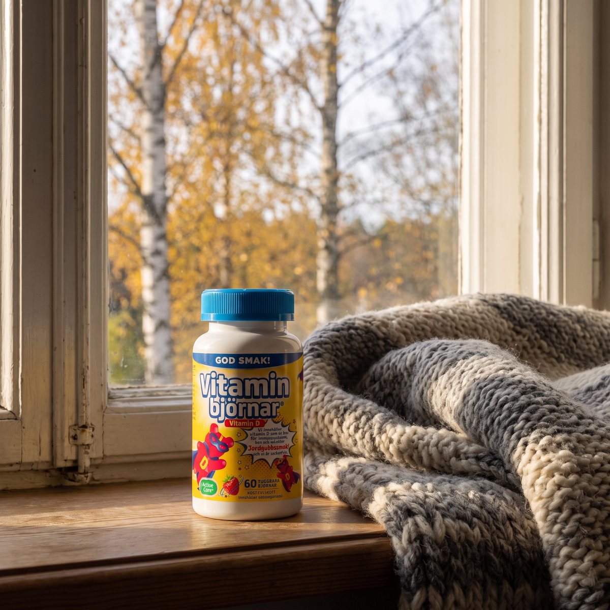 Active Care Vitaminbjörnar D-vitamin på ett fönsterbräde med björkar i höstfärger utanför