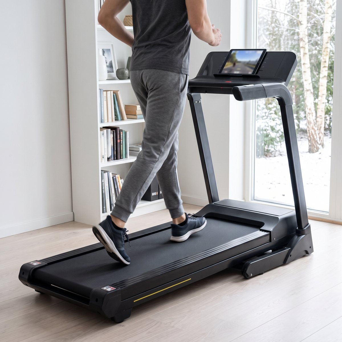 Svart Titan Life Delta T30-löpband med en surfplatta på konsolen i ett ljust svenskt radhusrum med bokhylla och snöig trädgård