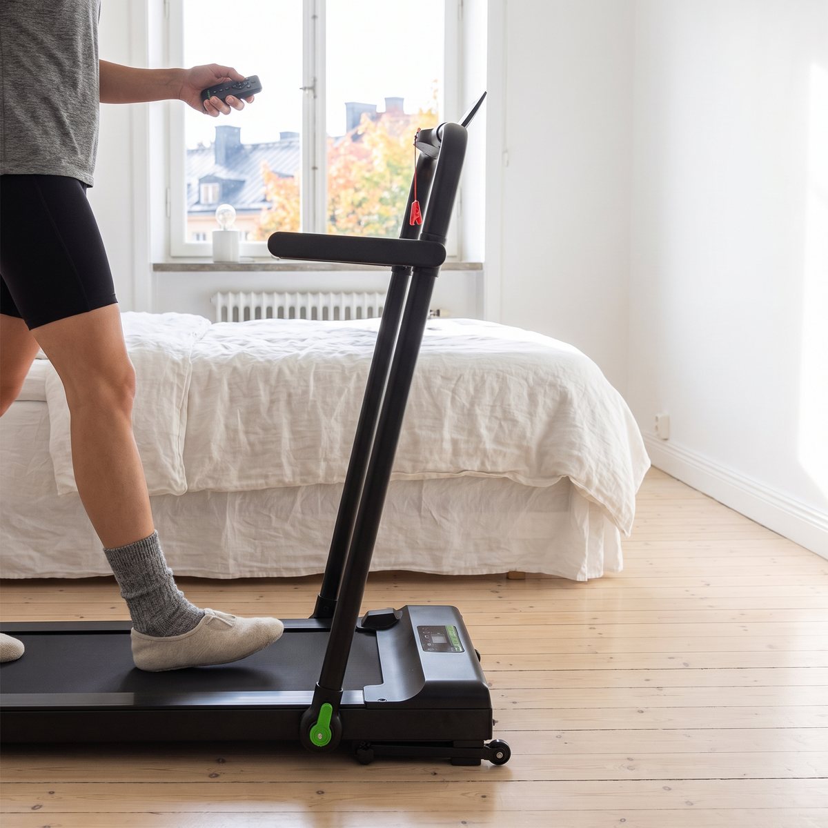 Smalt Tunturi Cardio Fit T10-löpband med gående som håller fjärrkontrollen, i ett ljust sovrum i en svensk lägenhet