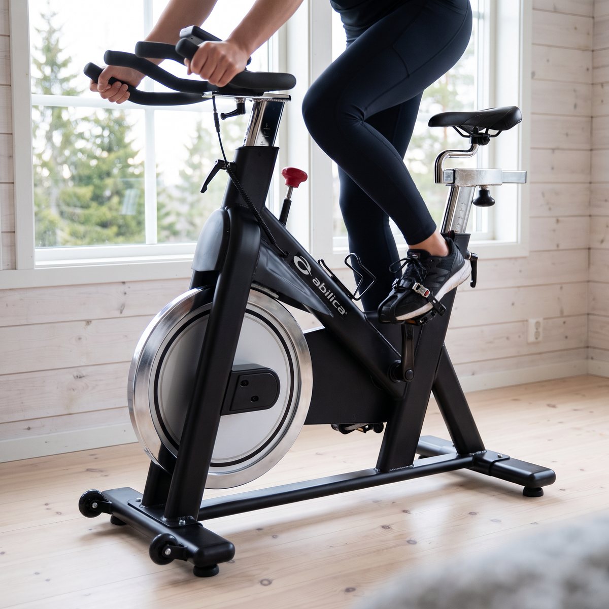 Abilica WinRacer spinningcykel i ett ljust svenskt hem med vitlaserade plankväggar och granar utanför fönstret