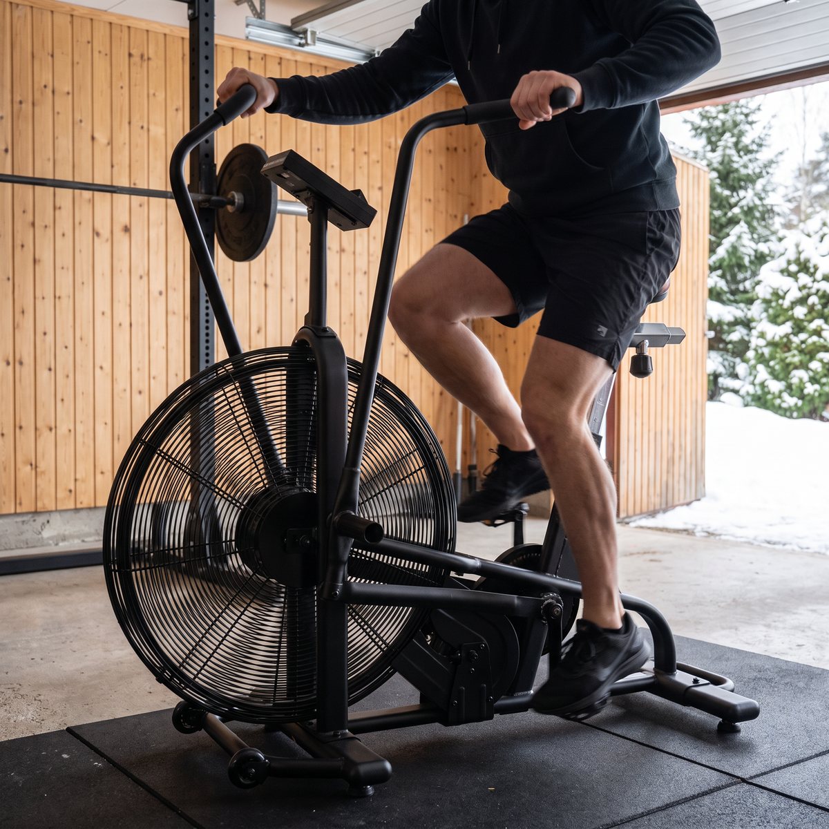 Assault AirBike Classic luftcykel i användning i ett garagegym med panelväggar och snöig vintertomt utanför den öppna porten