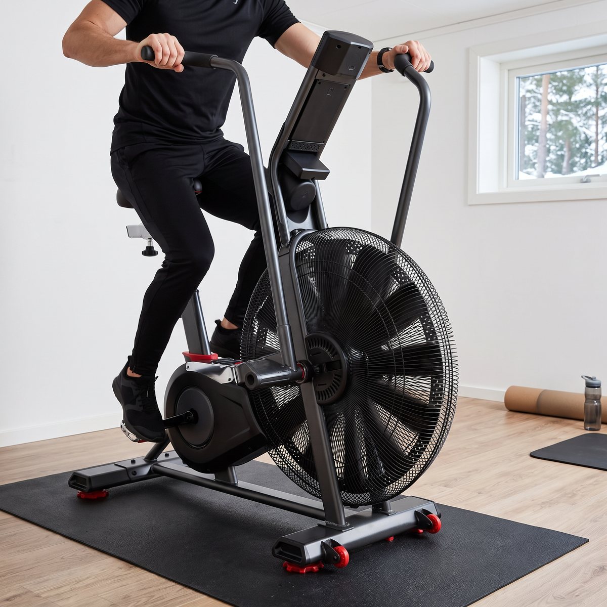 Schwinn Airdyne AD8 luftcykel i användning under ett intervallpass i ett källargym i en svensk villa med ljust trägolv och snöiga tallar utanför fönstret