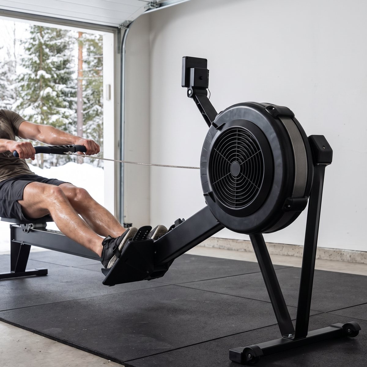 Master Fitness Nero Airrower med svart fläkthjul används på gummimattor i ett garage med snötäckta granar utanför