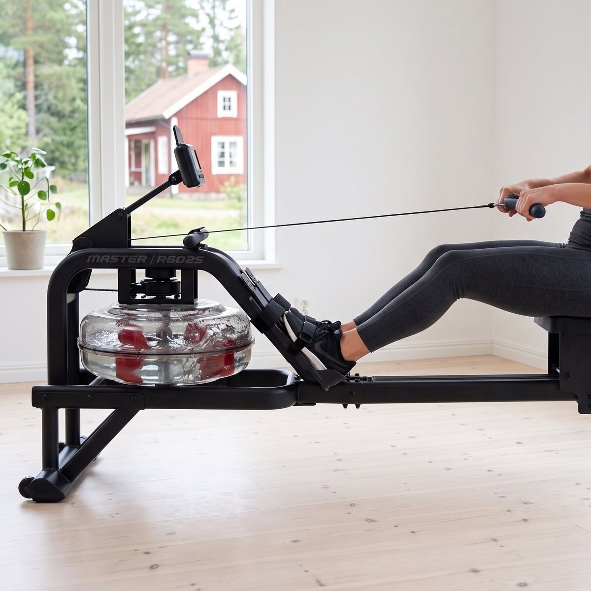 Master Fitness R6025 med vattentank och röda paddlar används i ett ljust rum med furugolv och ett rött trähus utanför fönstret
