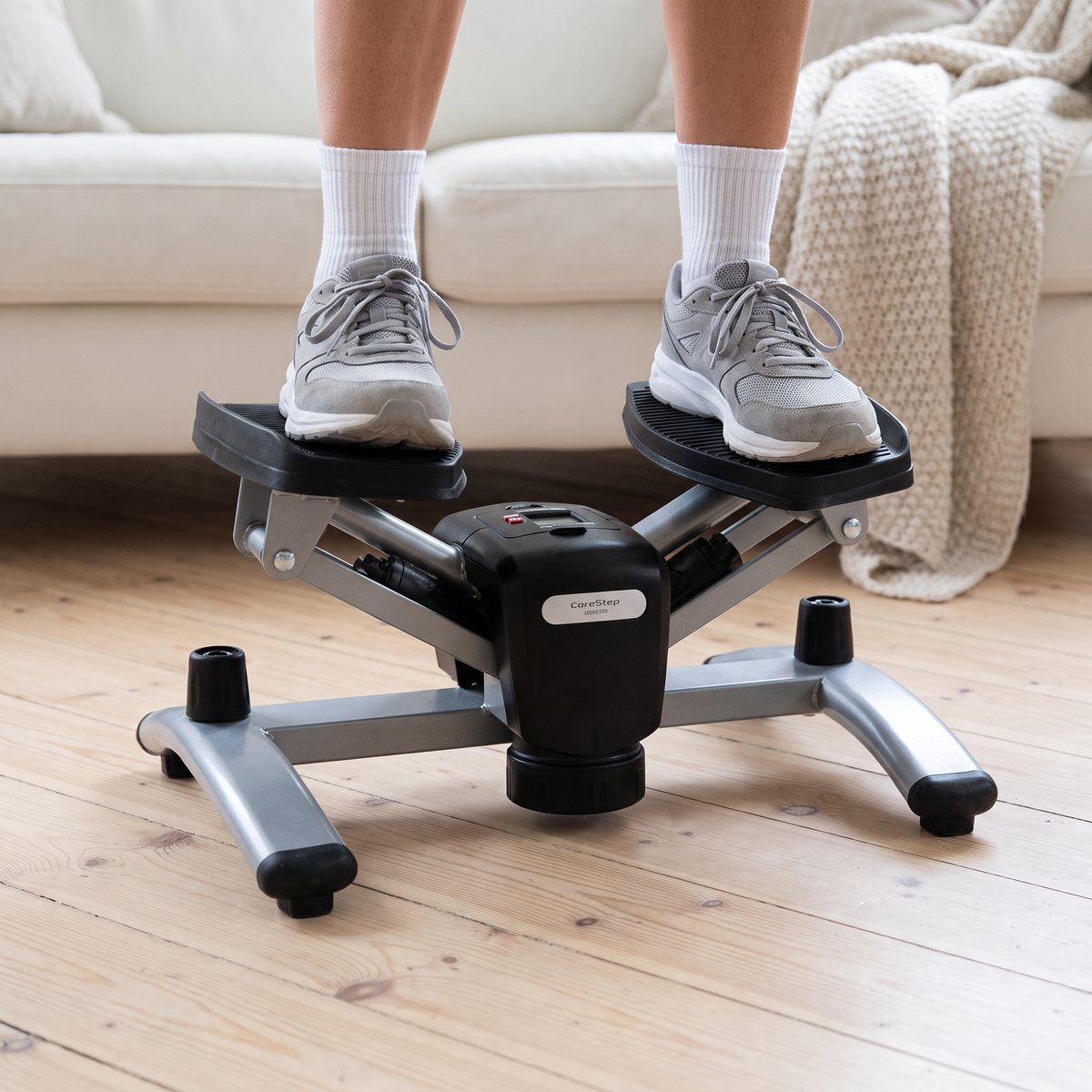 Abilica CoreStep 360 används av en person i vita strumpor och grå sneakers på trägolv framför en soffa i ett svenskt vardagsrum