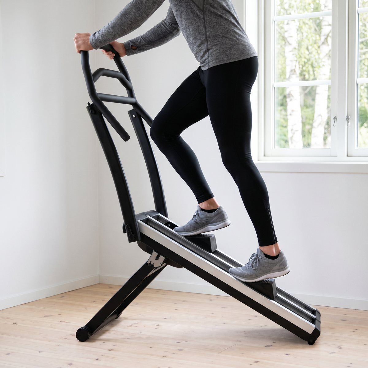 Abilica StairClimber 30 används av en person i träningskläder i ett ljust svenskt hemmagym med trägolv och björkar utanför fönstret