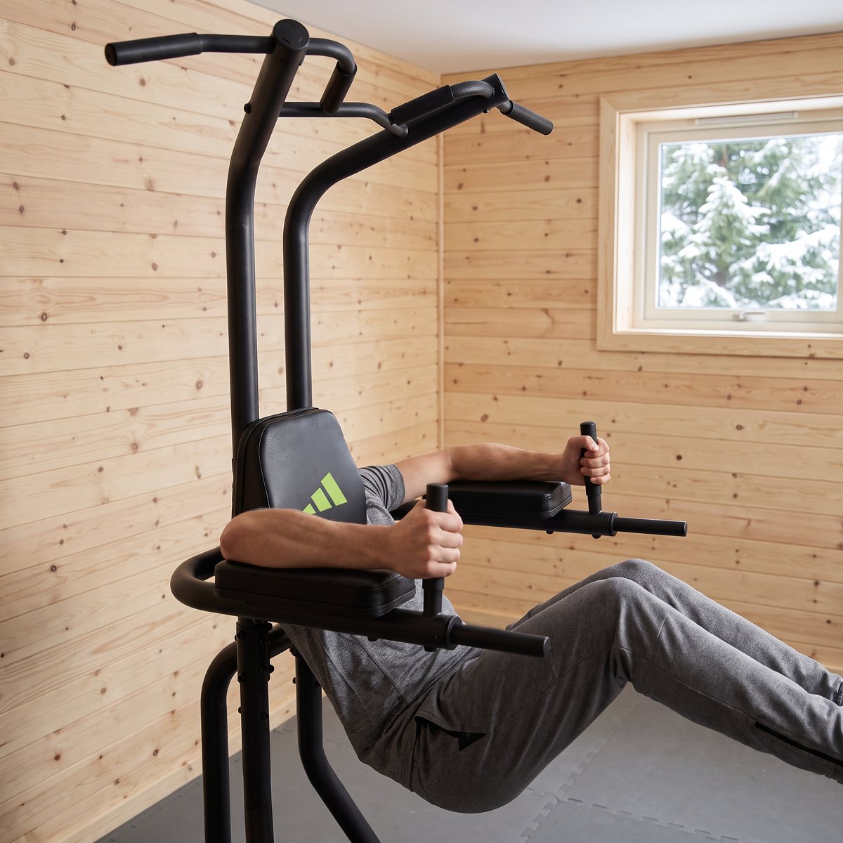 Adidas Performance Power Tower med en person som gör hängande benlyft med underarmarna på dynorna i ett svenskt hemmagym med ljusa träpaneler