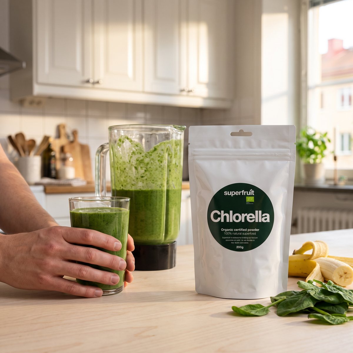 Vit påse med chlorellapulver bredvid en grön smoothie och spenat i ett ljust svenskt kök