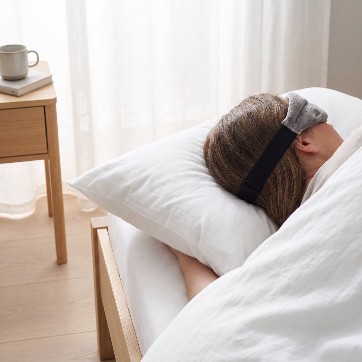 Person som sover på sidan i en ljus svensk sovrumsmiljö med grå Tempur-sovmask i velour och svart kardborreband över håret