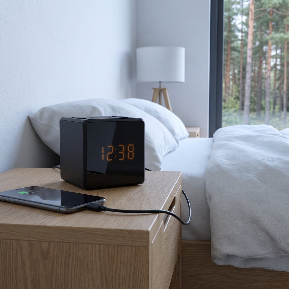 Svart kubformad klockradio Philips R4500 på ett nattduksbord i ek i ett ljust sovrum, med en mobil som laddas via sladd och tallskog utanför fönstret