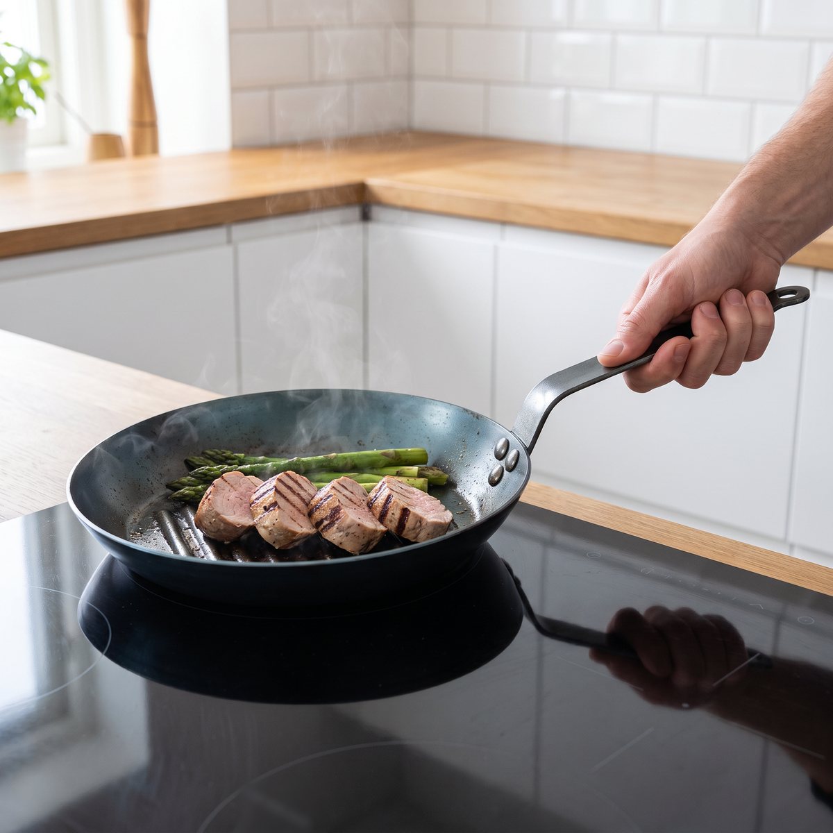 de Buyers runda grillpanna i kolstål med långt stålskaft, fläskfilé och sparris på en induktionshäll i ett svenskt kök