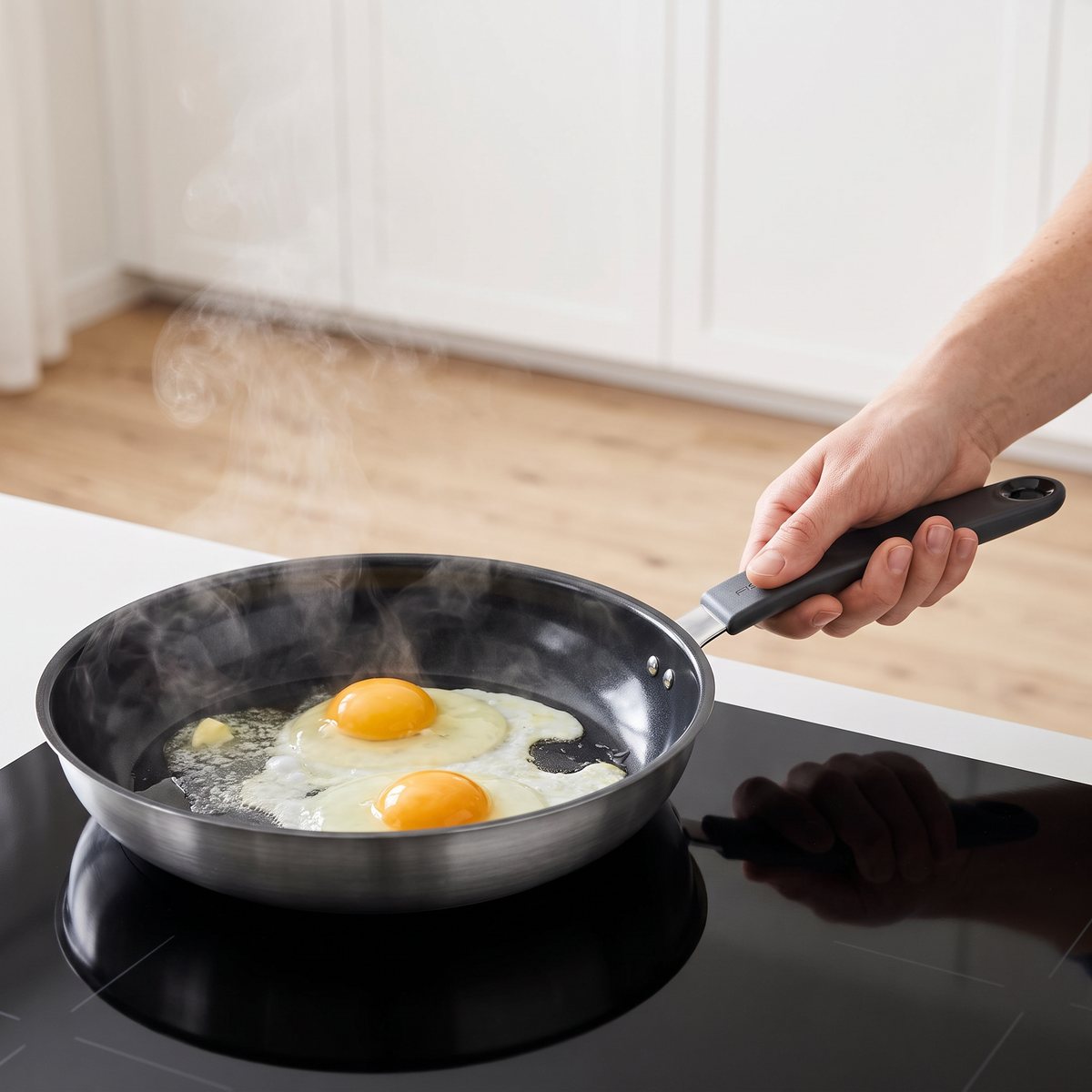 Keramisk stekpanna i rostfritt stål på induktionshäll i ett svenskt kök med stekta ägg