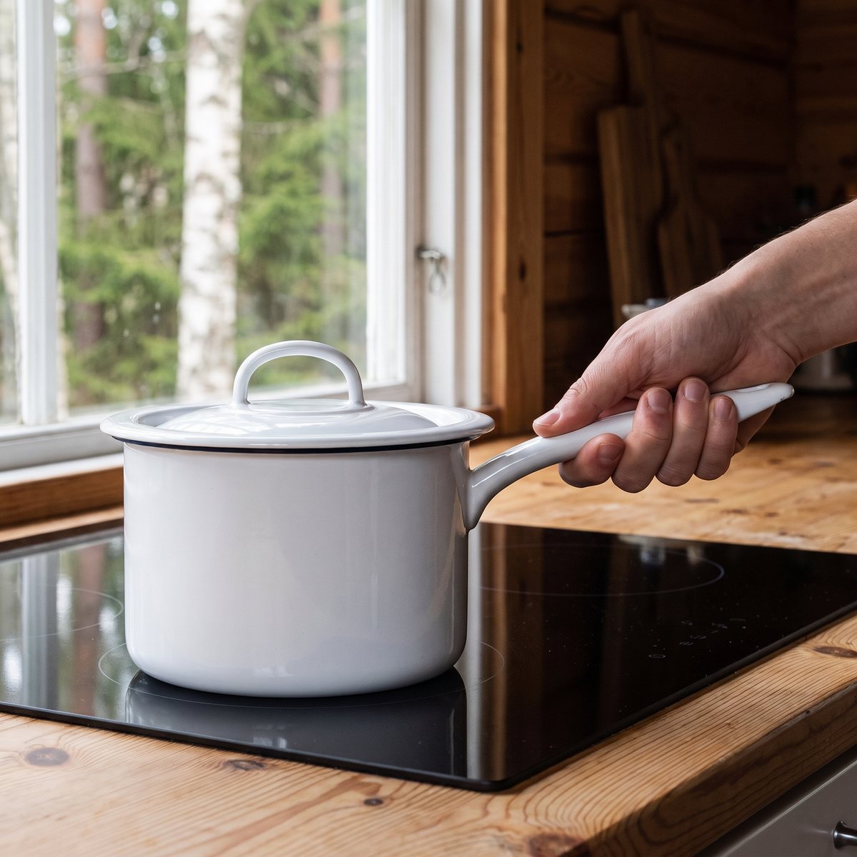Vit emaljkastrull med lock på en induktionshäll i ett svenskt kök