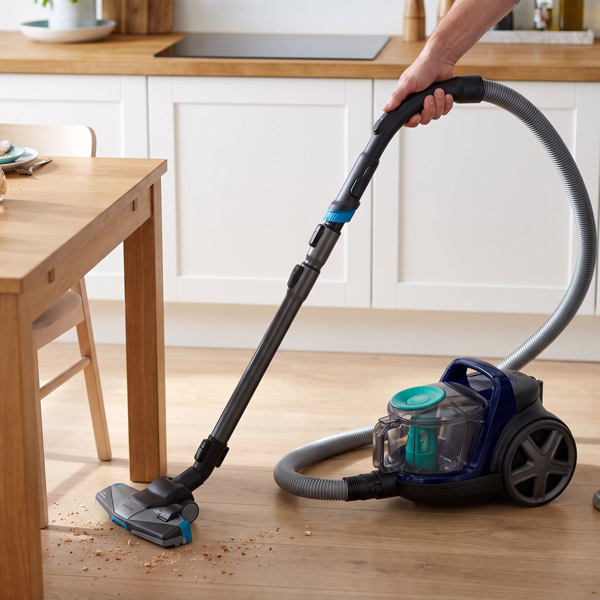 Mörkblå påslös Philips PowerPro Active suger upp brödsmulor under köksbordet i ett svenskt kök med induktionshäll