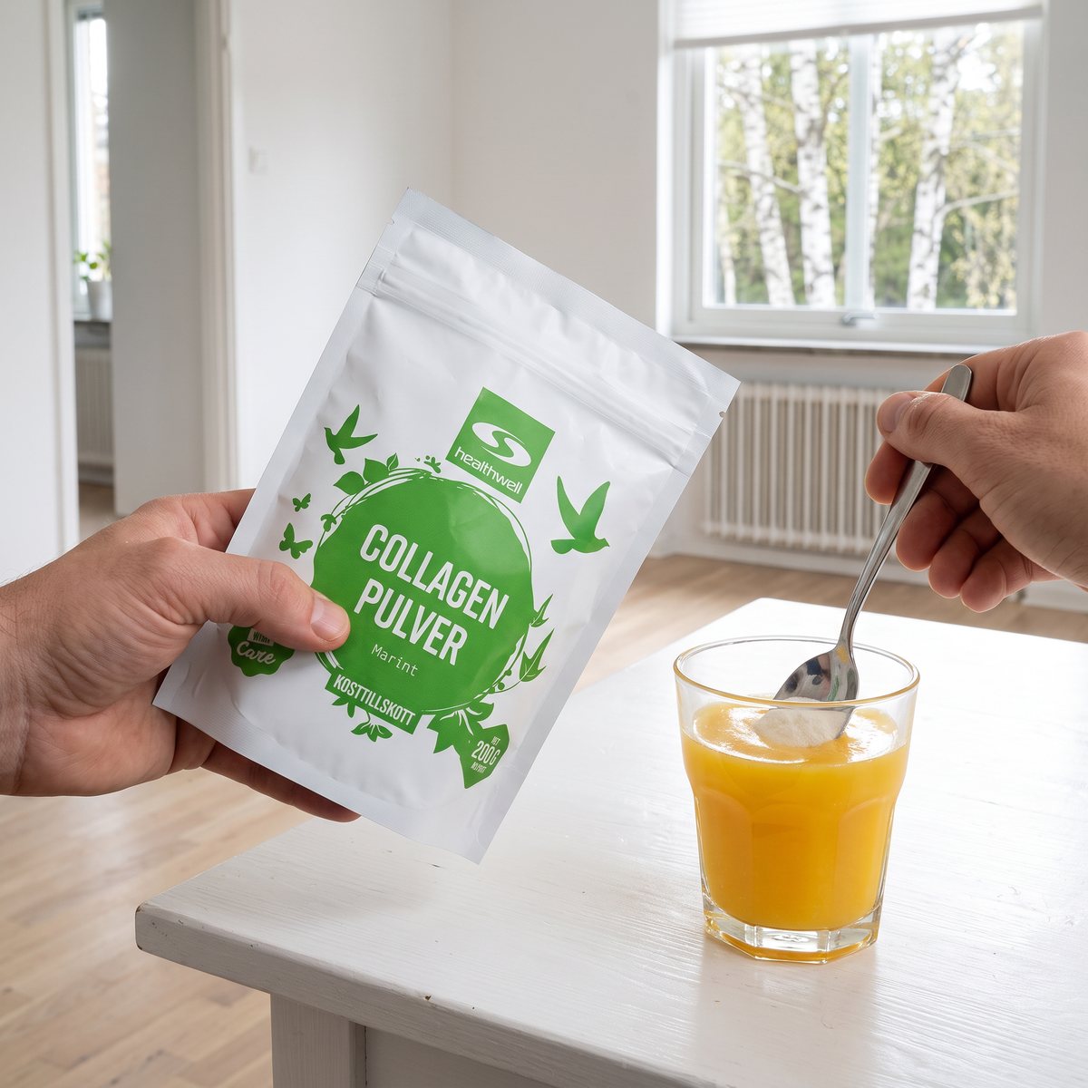 Healthwell Collagen Pulver Marint-påse hållen i handen vid ett vitt köksbord med ett glas juice i en svensk lägenhet