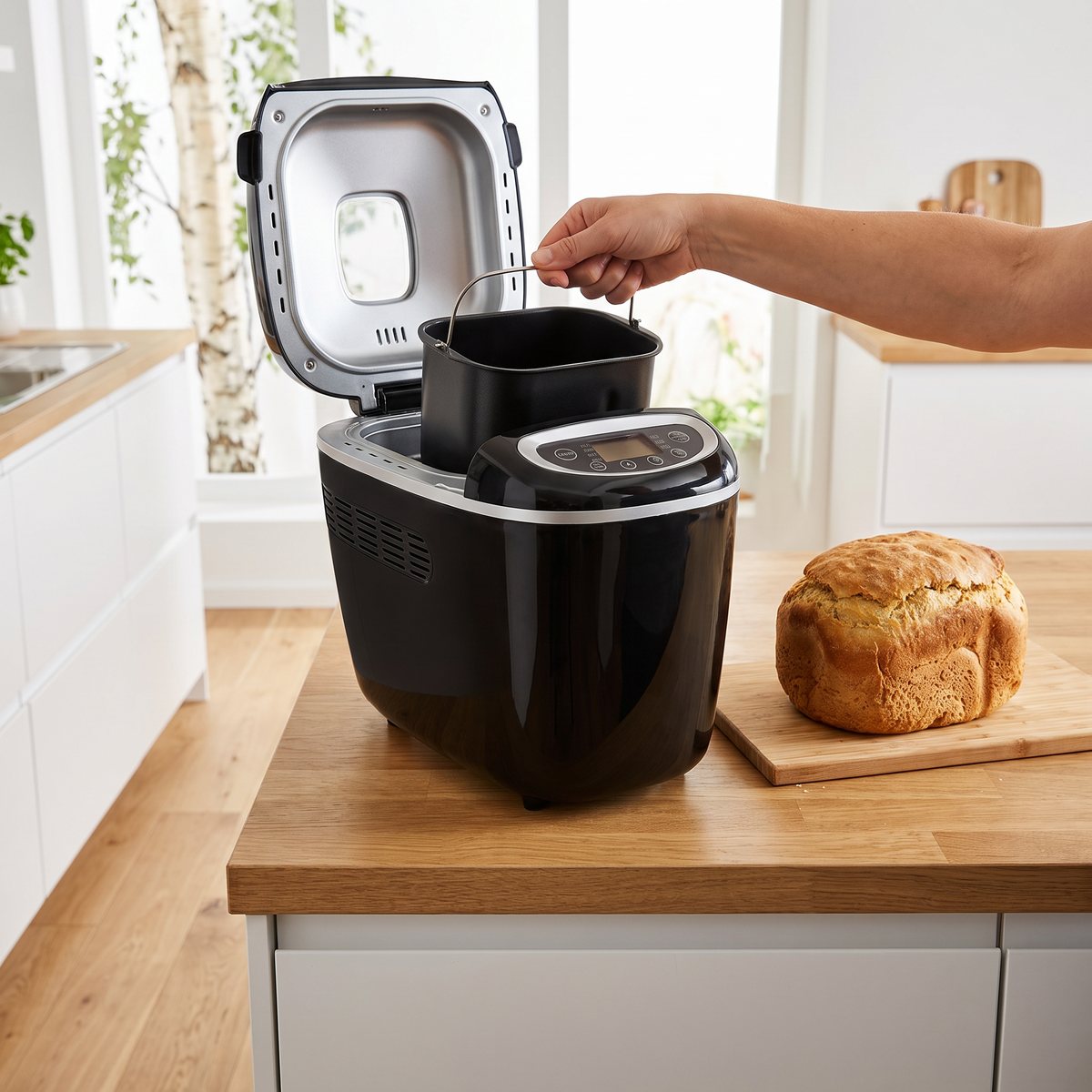 Svart brödbakmaskin från Tefal på en köksö i trä i ett svenskt kök, där en hand lyfter upp bakformen och ett nybakat bröd står på skärbrädan