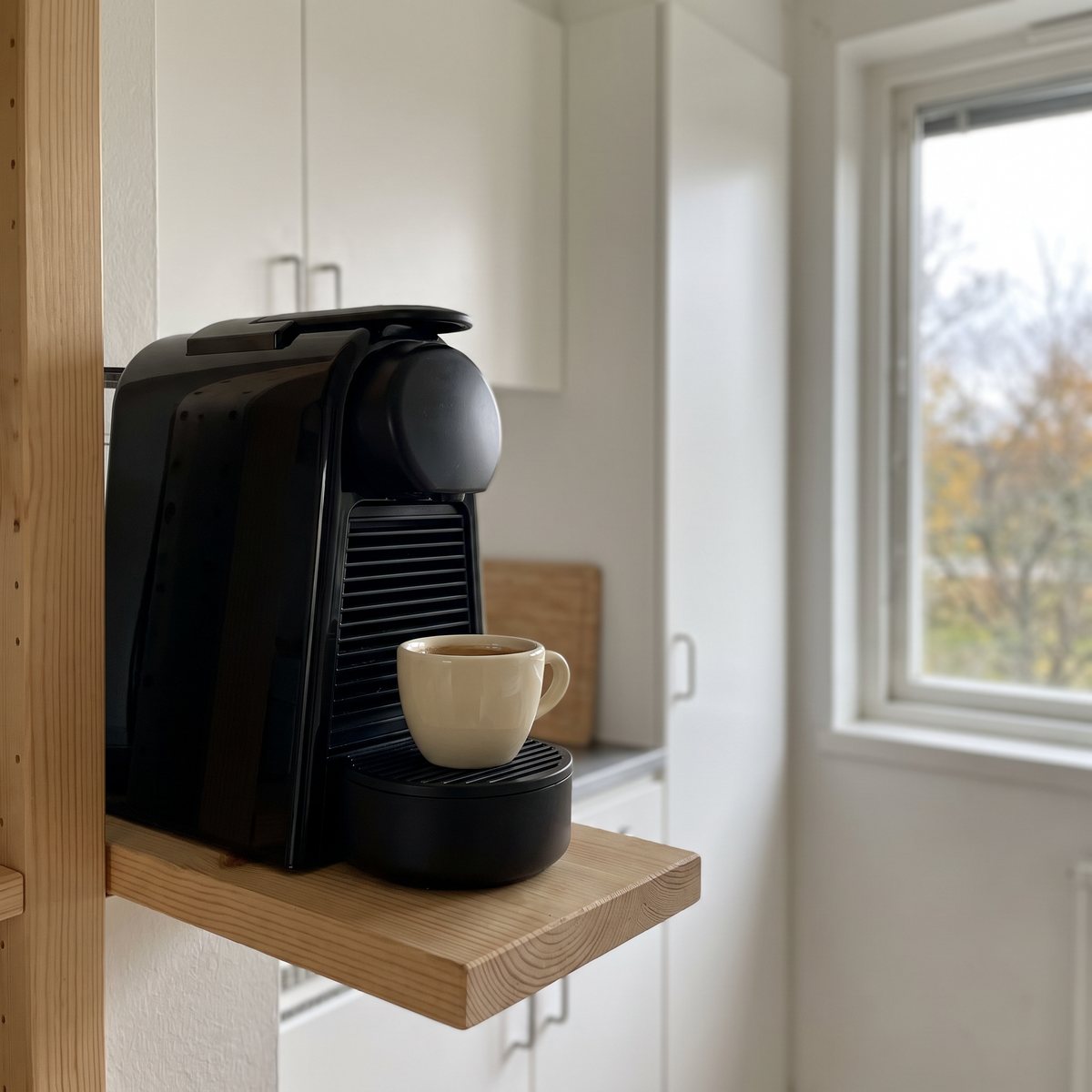 Svart Nespresso Essenza Mini på en hylla i ett litet svenskt kök med espressokopp under pipen