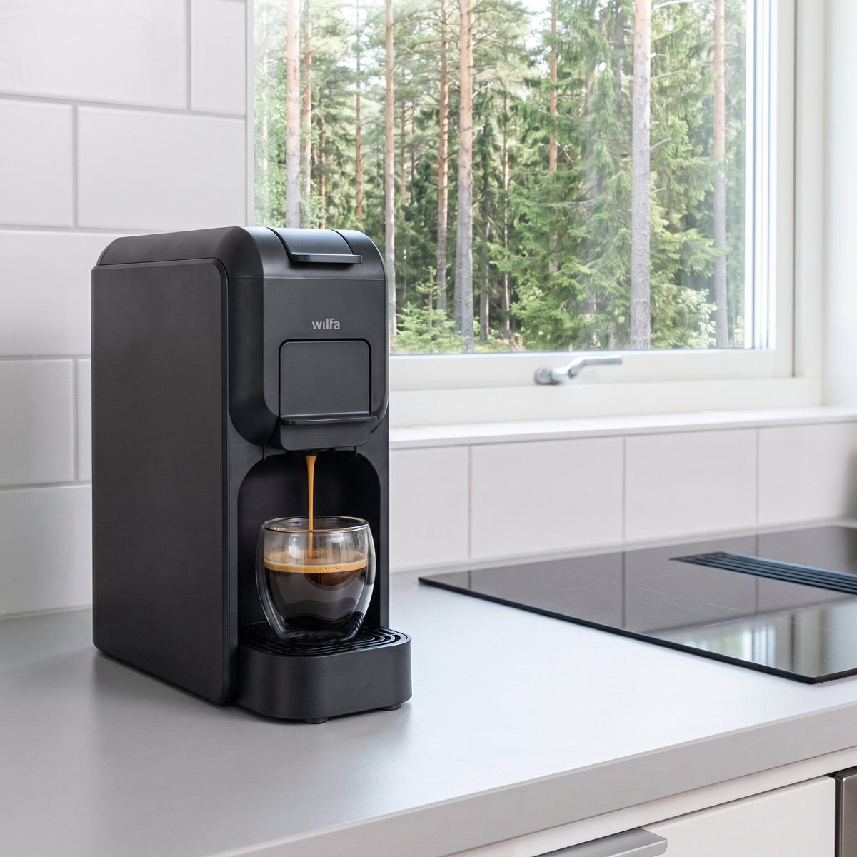Mörkgrå Wilfa Volo Capsule Mini som brygger espresso i ett svenskt kök med utsikt över tallskog