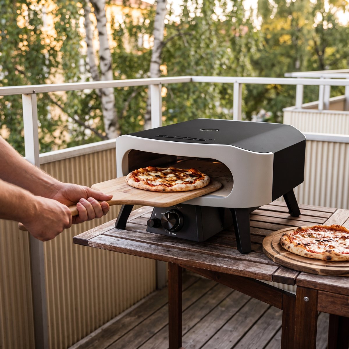 Pizzaugnen Cozze Classic på ett bord på en svensk balkong med pizza som gräds