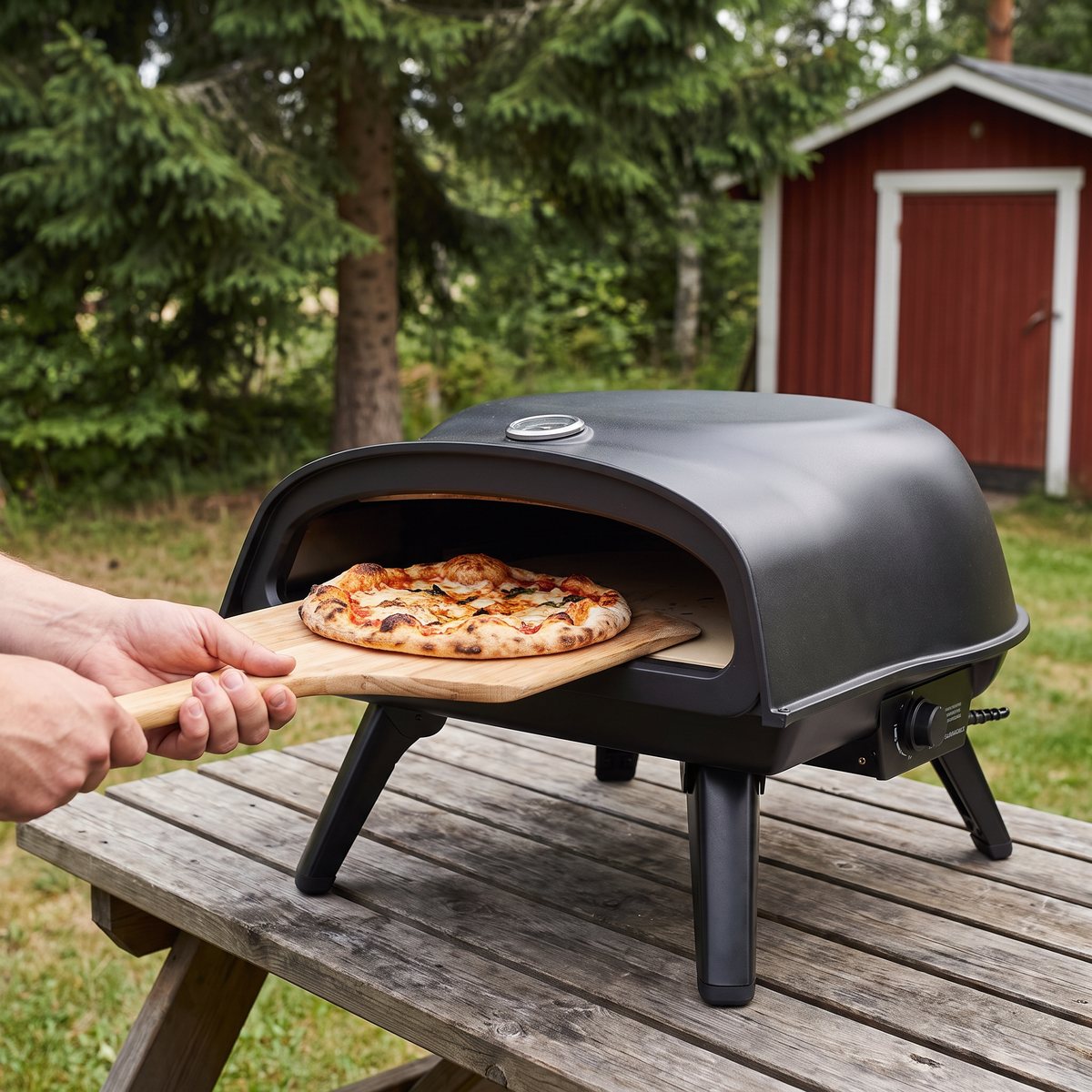 Muurikka pizzaugn för gasol på ett utebord i en svensk sommarträdgård med en pizza på spade