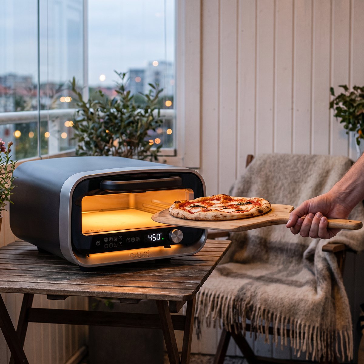 Elektriska pizzaugnen Ooni Volt 2 på ett bord på en inglasad balkong med en pizza på spade