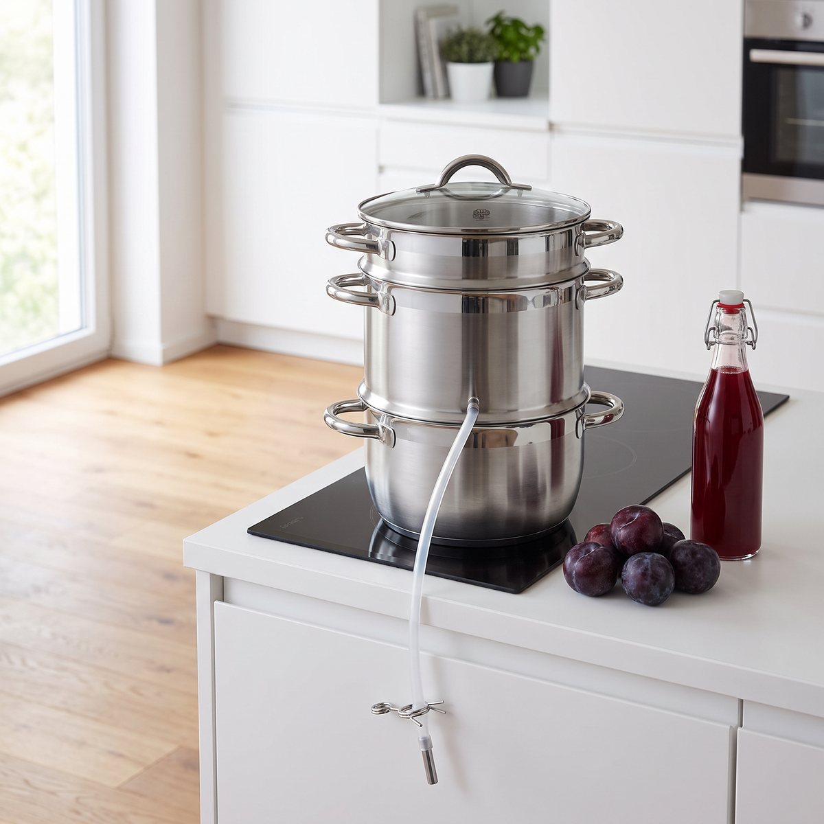 Rostfri ångsaftkokare på en induktionshäll i ett modernt svenskt kök med plommon och en flaska saft