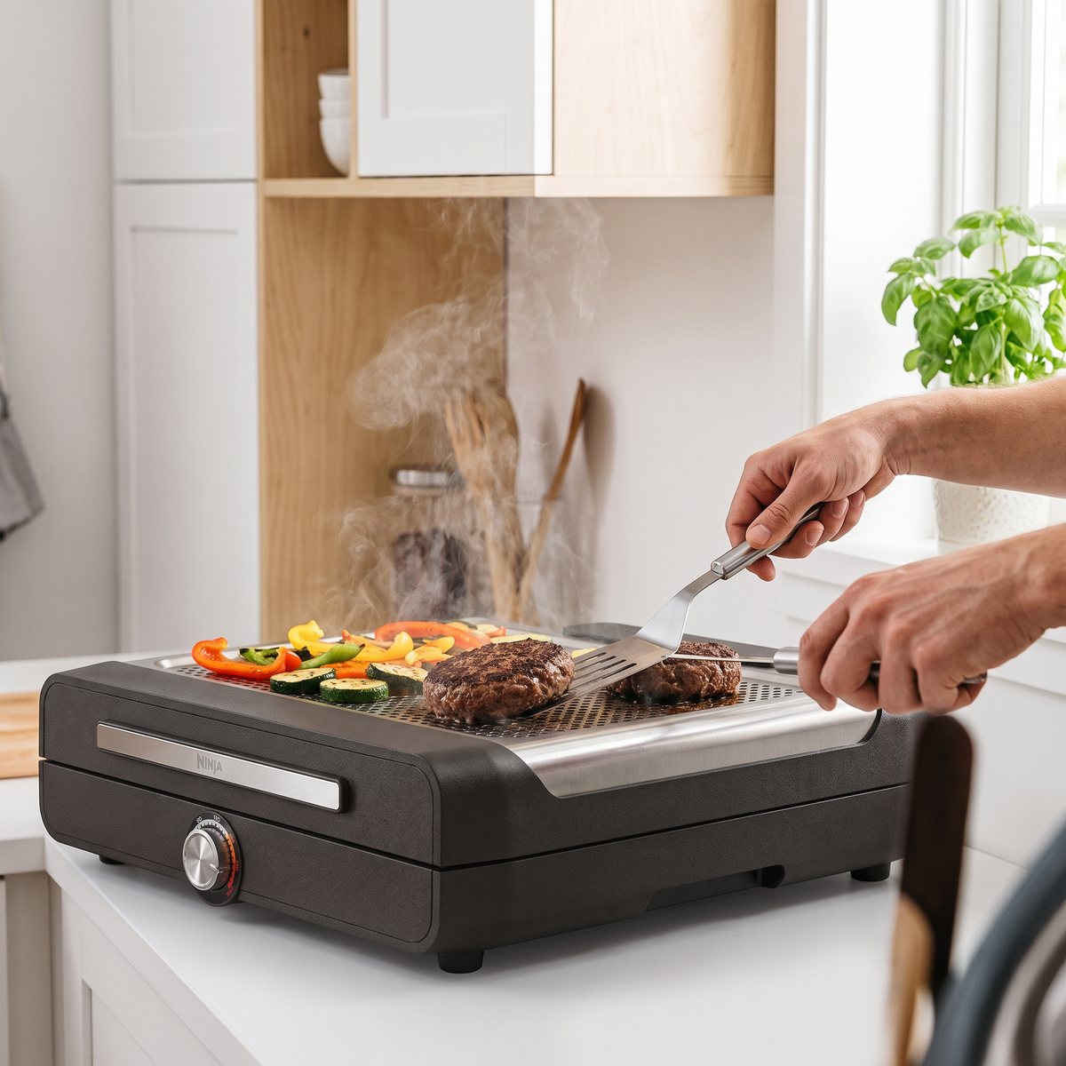 Ninja Sizzle GR101EU kontaktgrill på en vit köksbänk i ett svenskt kök, med hamburgare och grönsaker på grillplattan