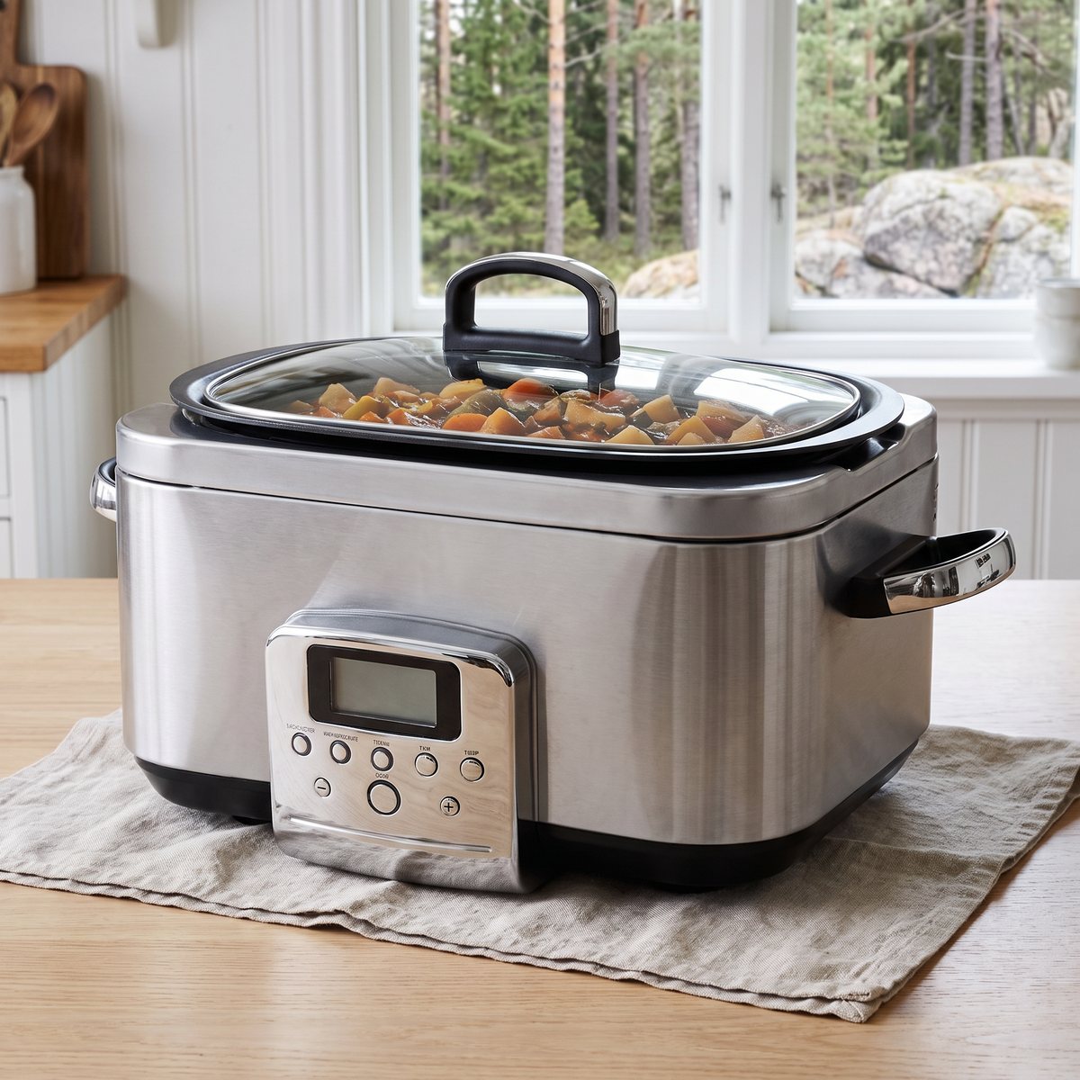 GreenPan Elite slow cooker i rostfritt stål med grytan synlig genom glaslocket på ett träbord i ett svenskt kök