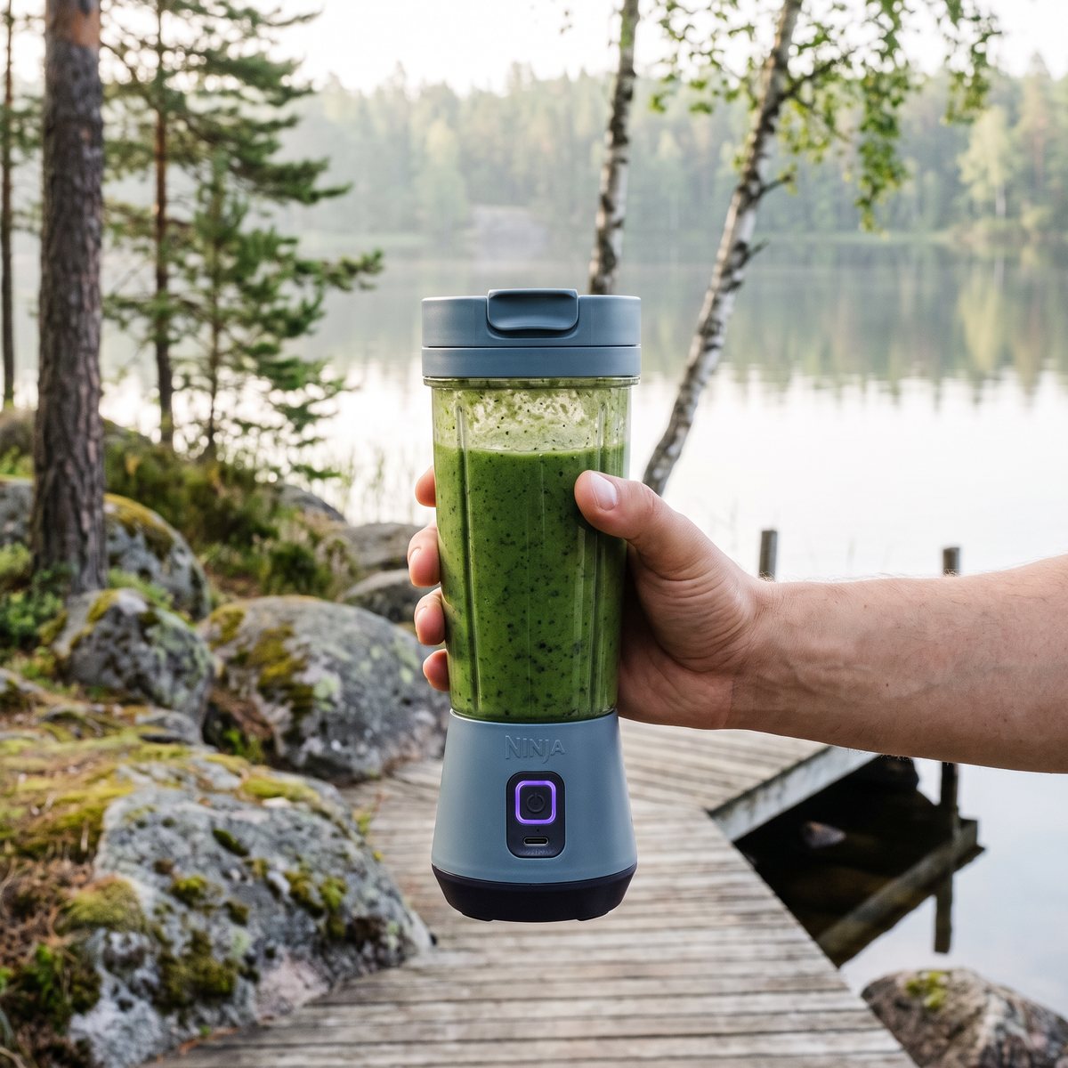 Hand håller Ninja Blast portabel blender med grön smoothie på en brygga vid en svensk sjö