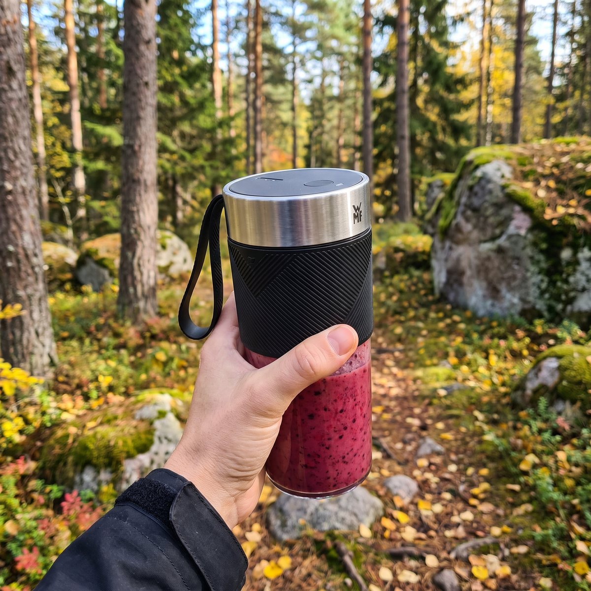 Hand håller WMF Kitchen Minis blender med bärsmoothie på en stig i svensk höstskog