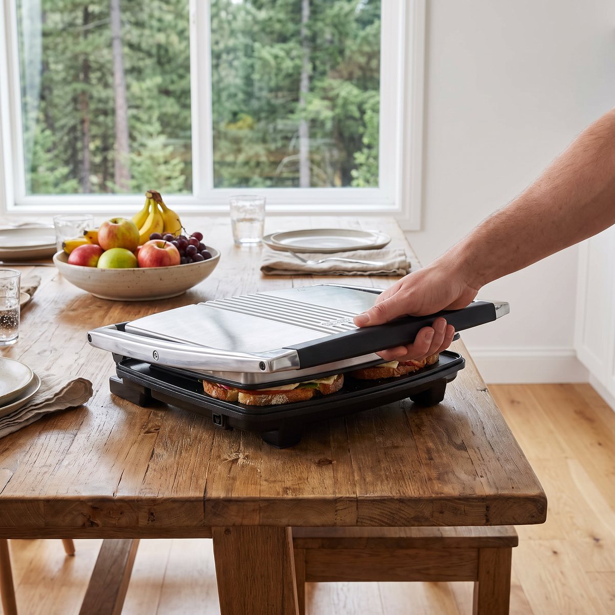 Breville Paninigrill 4 skivor där en hand trycker ned handtaget över en macka vid ett svenskt köksbord