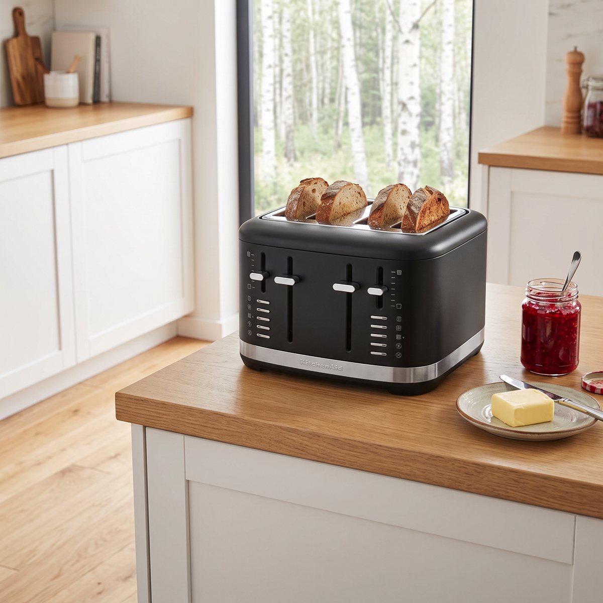 Svart KitchenAid-brödrost med fyra fack och reglage på en träbänk i ett svenskt kök med björkar utanför fönstret