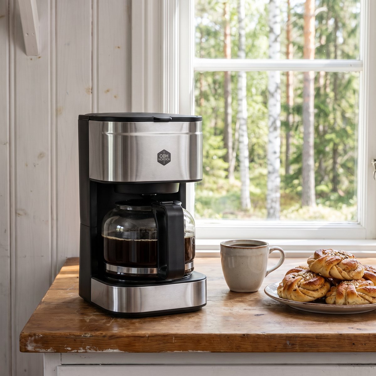 OBH Nordica Coffee Prio på en bänk i ett svenskt sommarstugekök med björkar utanför fönstret