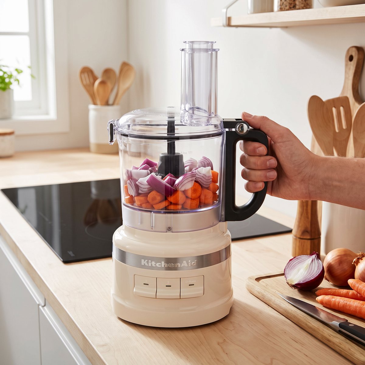 KitchenAid 5KFP0719 i cremefärg som hackar lök och morötter på en träbänk i ett svenskt kök med induktionshäll