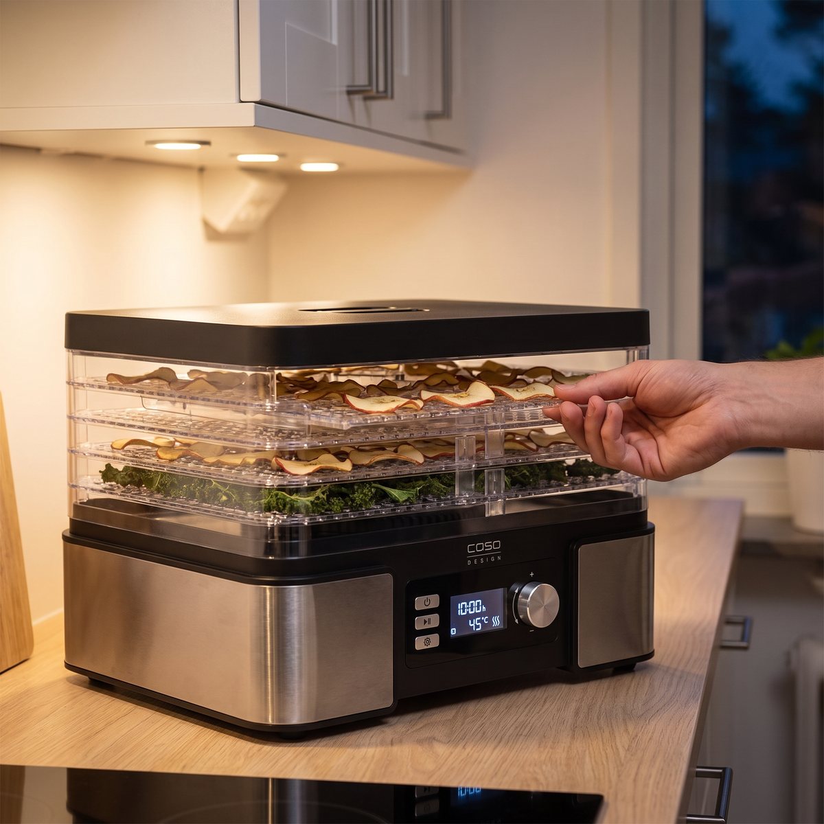 Caso DH 450 med belyst display och äppelchips på brickorna, under ett väggskåp i ett svenskt kök en kväll