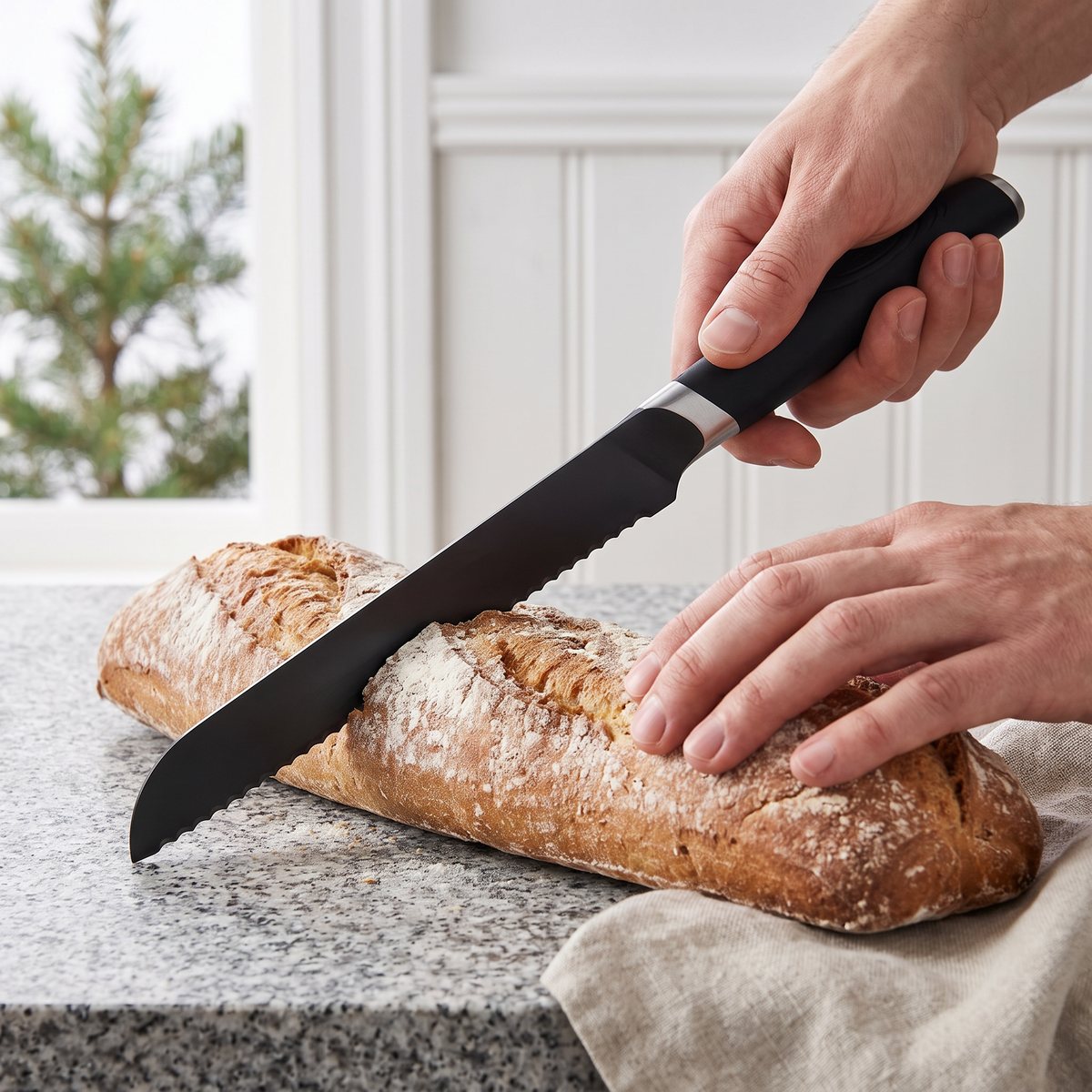 Onyx Cookware brödkniv som delar en lantbaguette på en granitbänk i ett svenskt stugkök