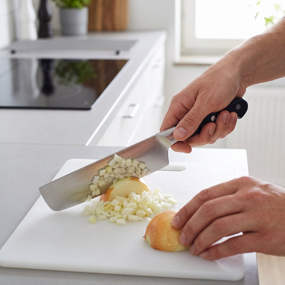 Zwilling Pro Nakiri med rakt stålblad och svart handtag med nitar hackar gul lök på en vit skärbräda i ett svenskt kök med induktionshäll