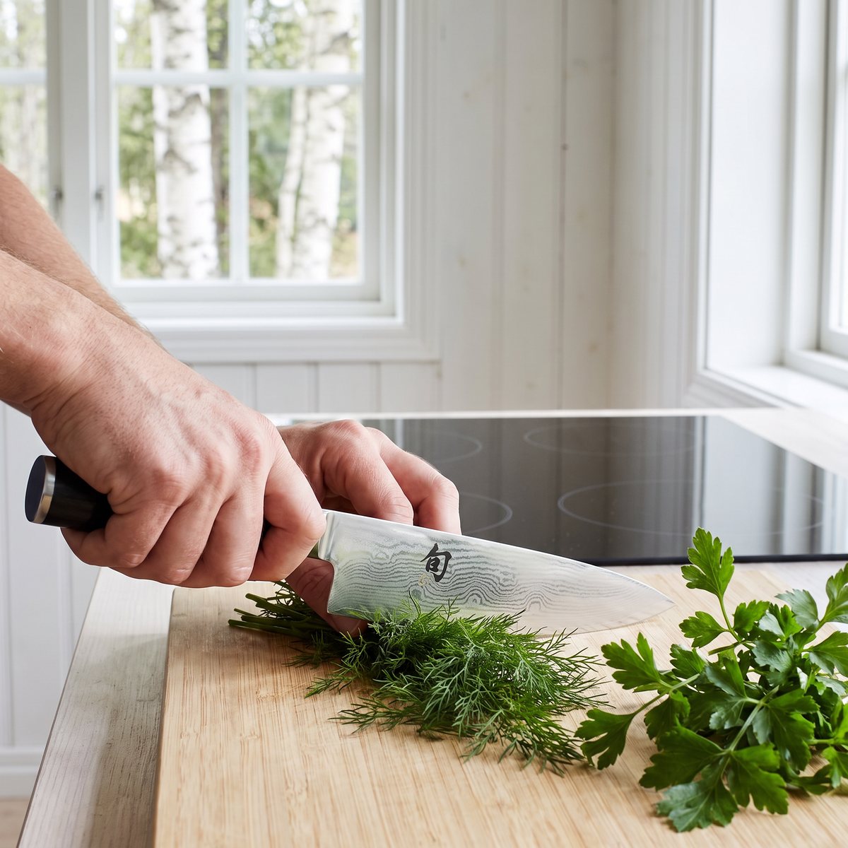 Kai Shun Classic kockkniv hackar dill och persilja i ett ljust svenskt lanthusköken med björkar utanför fönstret