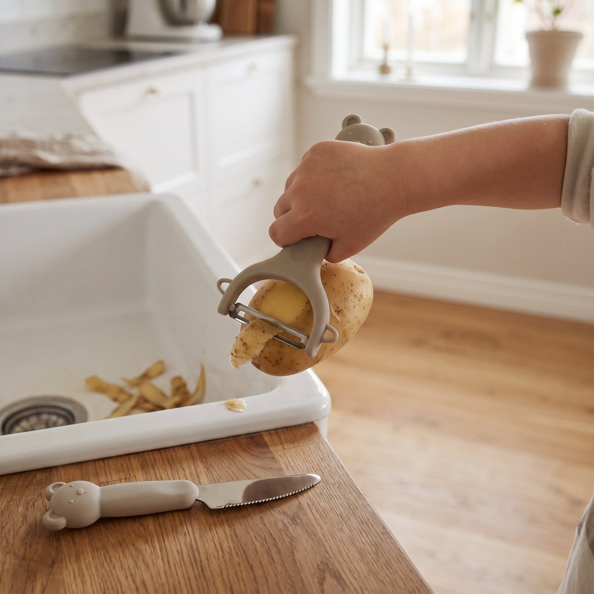 Barn som skalar potatis med Liewood Pertense skalare, kniven ligger på skärbrädan i ett svenskt kök
