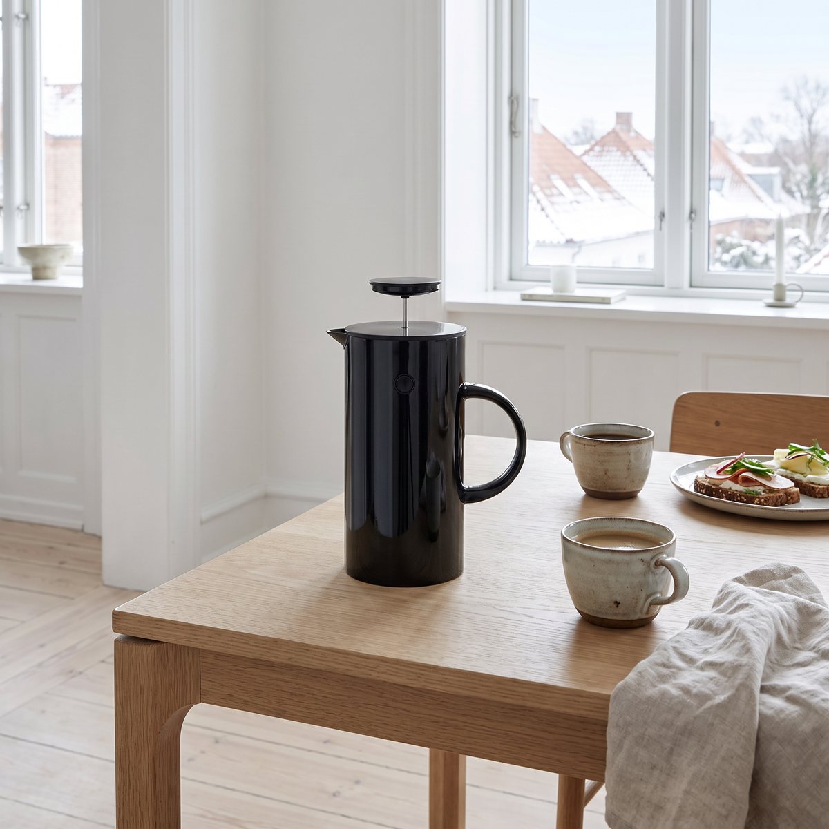 Svart Stelton EM kaffepress på ett ekbord dukat för frukost med kaffekoppar och smörgåsar i en ljus svensk lägenhet en vinterdag