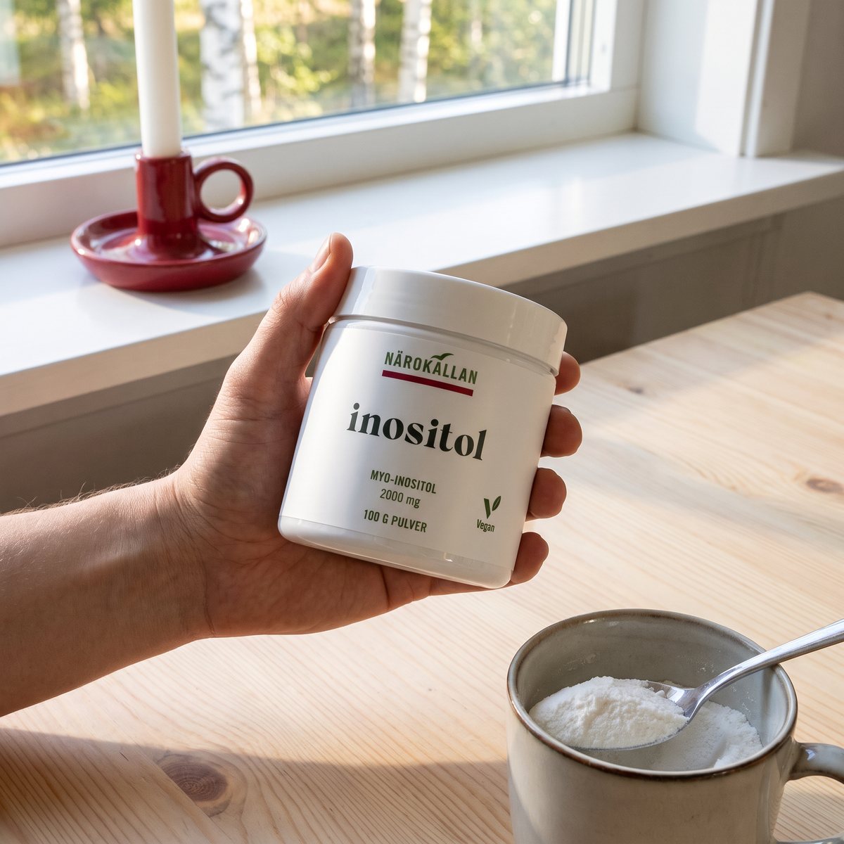 Närokällan Inositol i vit burk hållen över en kopp vid ett frukostbord i ett svenskt hem