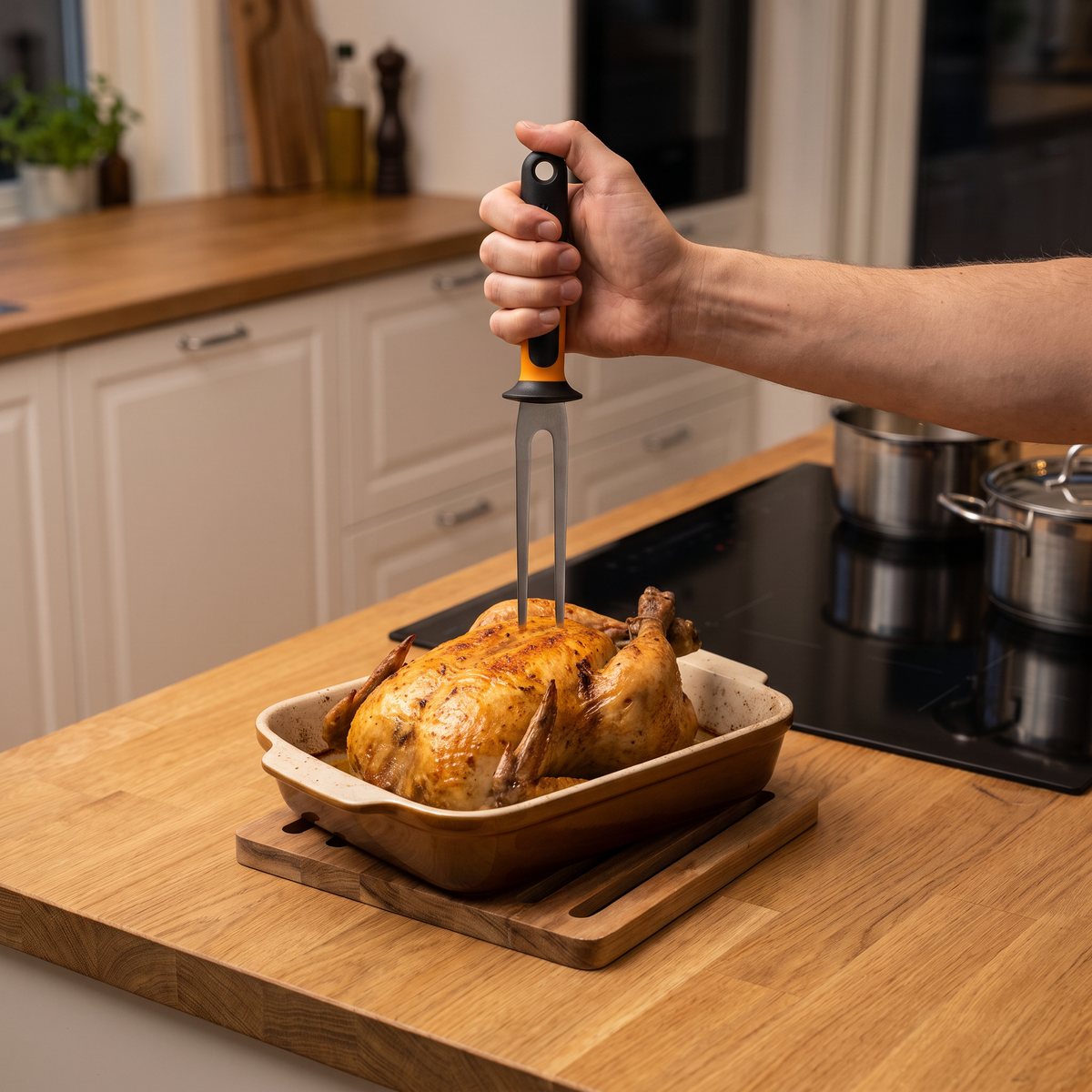 Fiskars Functional Form stekgaffel i en ugnsstekt kyckling i en form på köksbänken i ett svenskt kök med induktionshäll