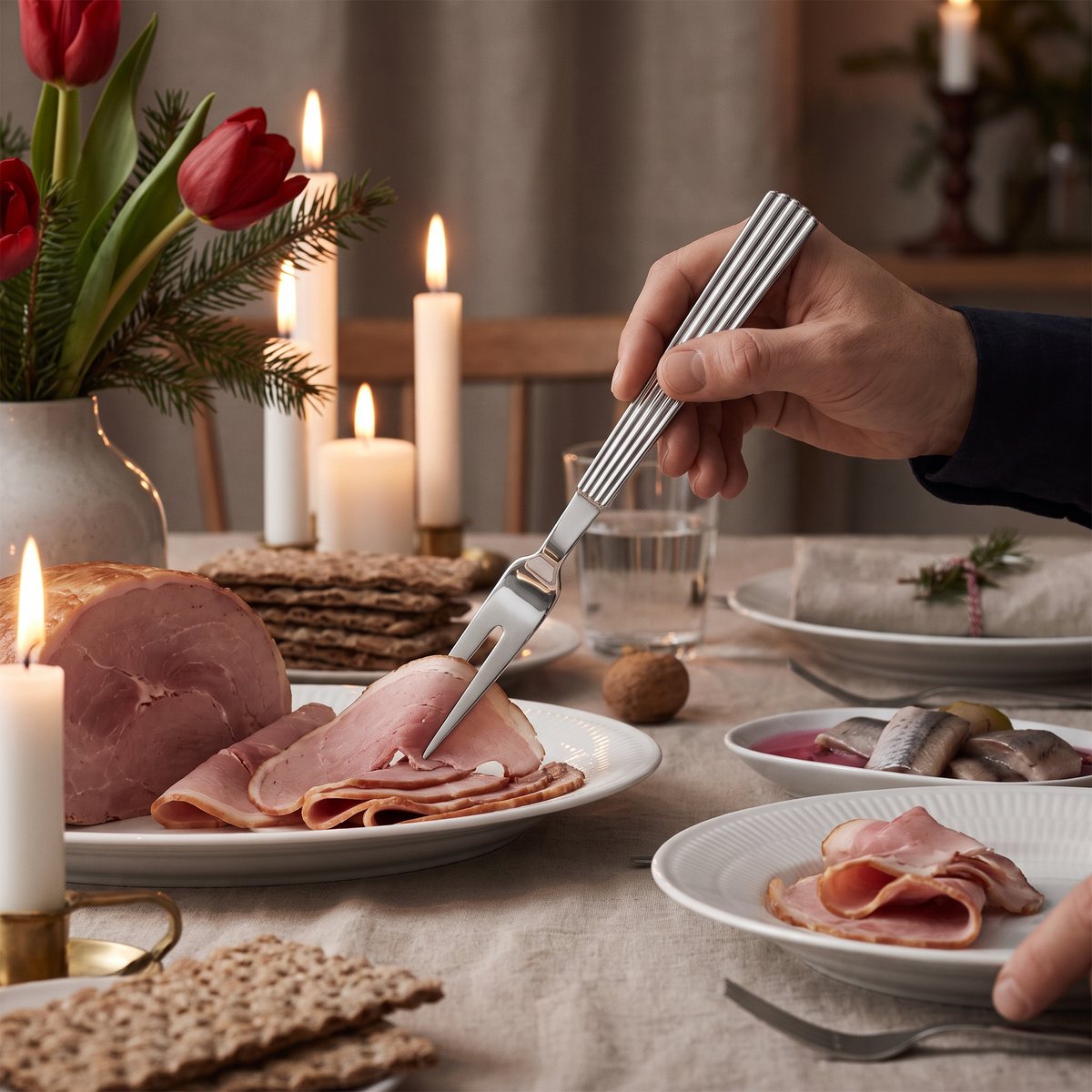Georg Jensen Bernadotte köttgaffel lägger upp skivad julskinka på ett svenskt julbord med tända ljus och tulpaner