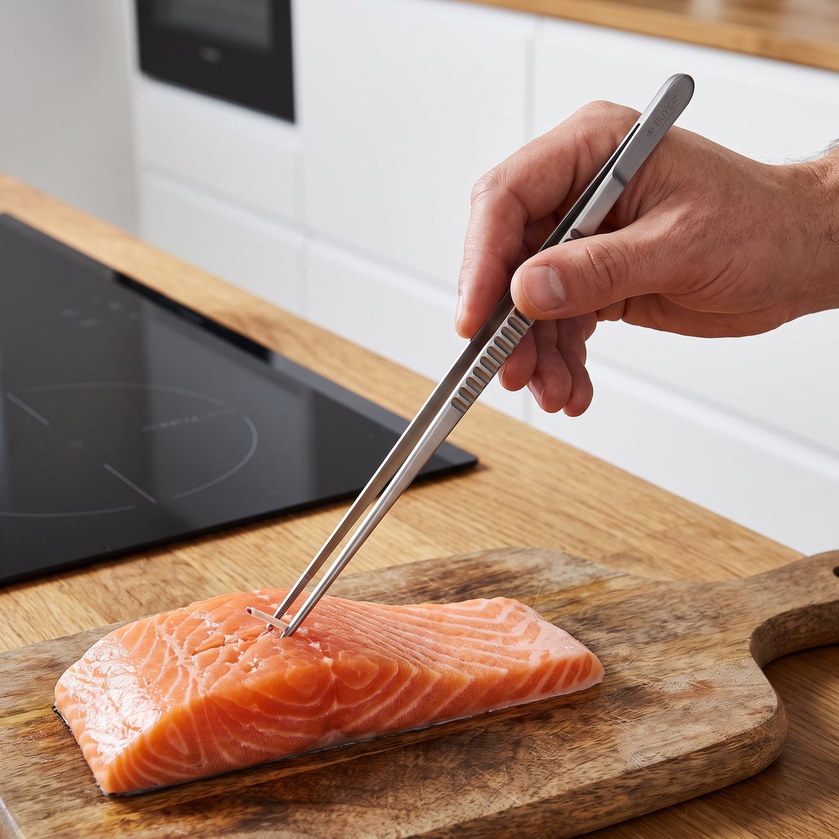 De Buyer pincett i rostfritt stål som drar ut en fiskben ur en fiskfilé på en skärbräda i ett svenskt kök