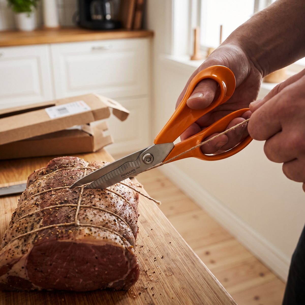 Fiskars TX45 med orange handtag som klipper garn runt en stek på en bänk i ett svenskt kök