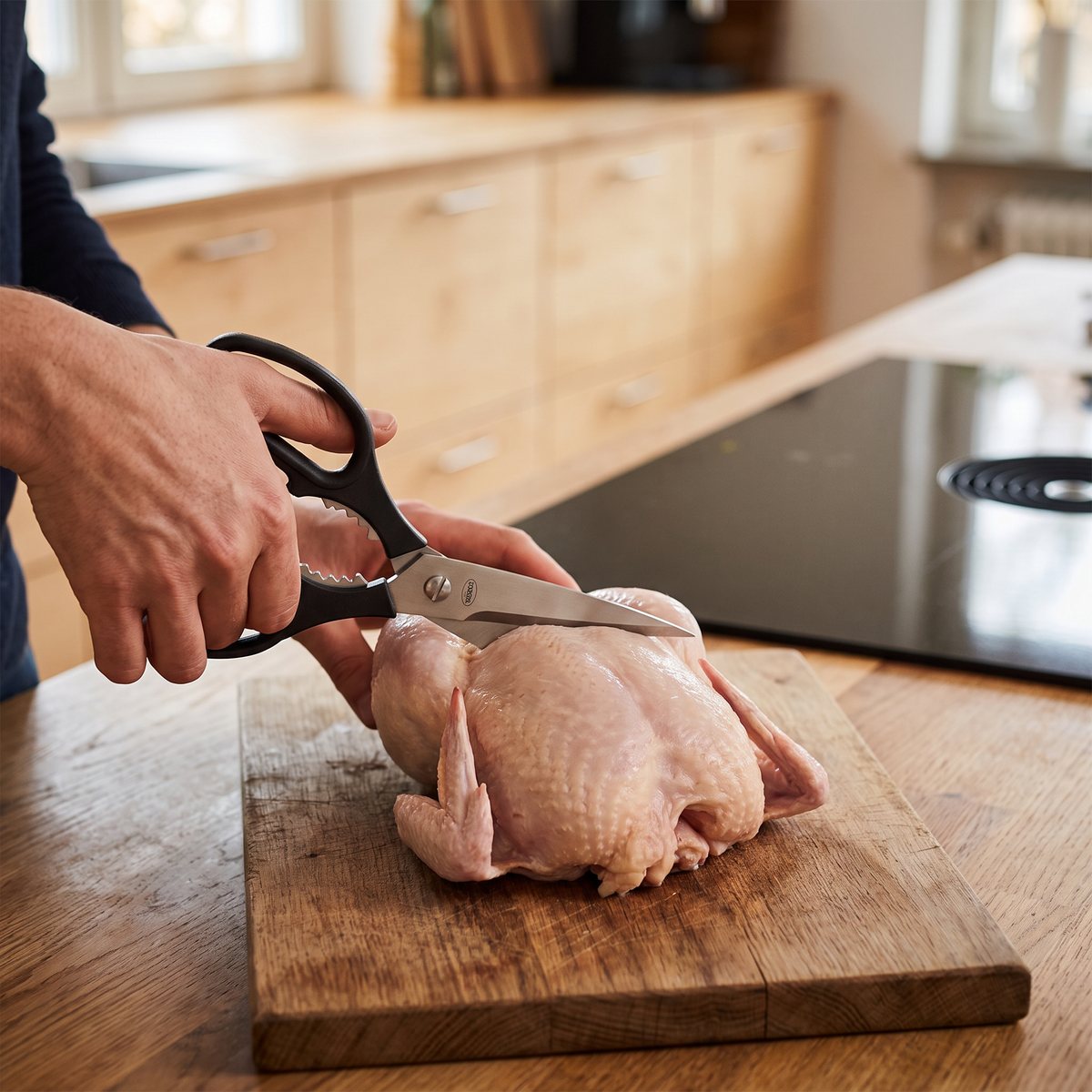 Rösle kökssax med svarta handtag som delar en rå kyckling på en träskiva i ett svenskt kök