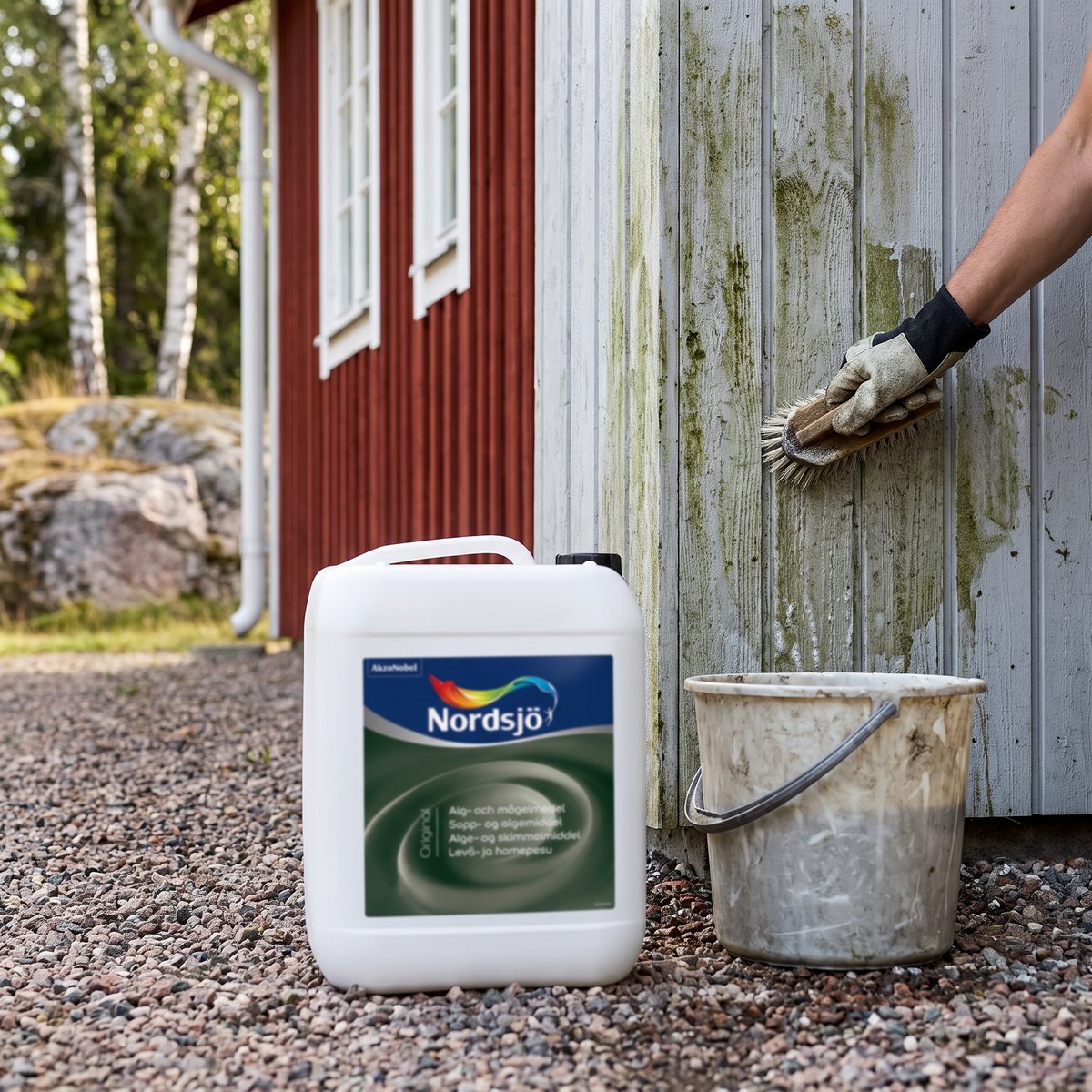 Nordsjö Original Alg- och mögelmedel 5 l på en grusgång medan medlet borstas in i en grå träpanel med påväxt.