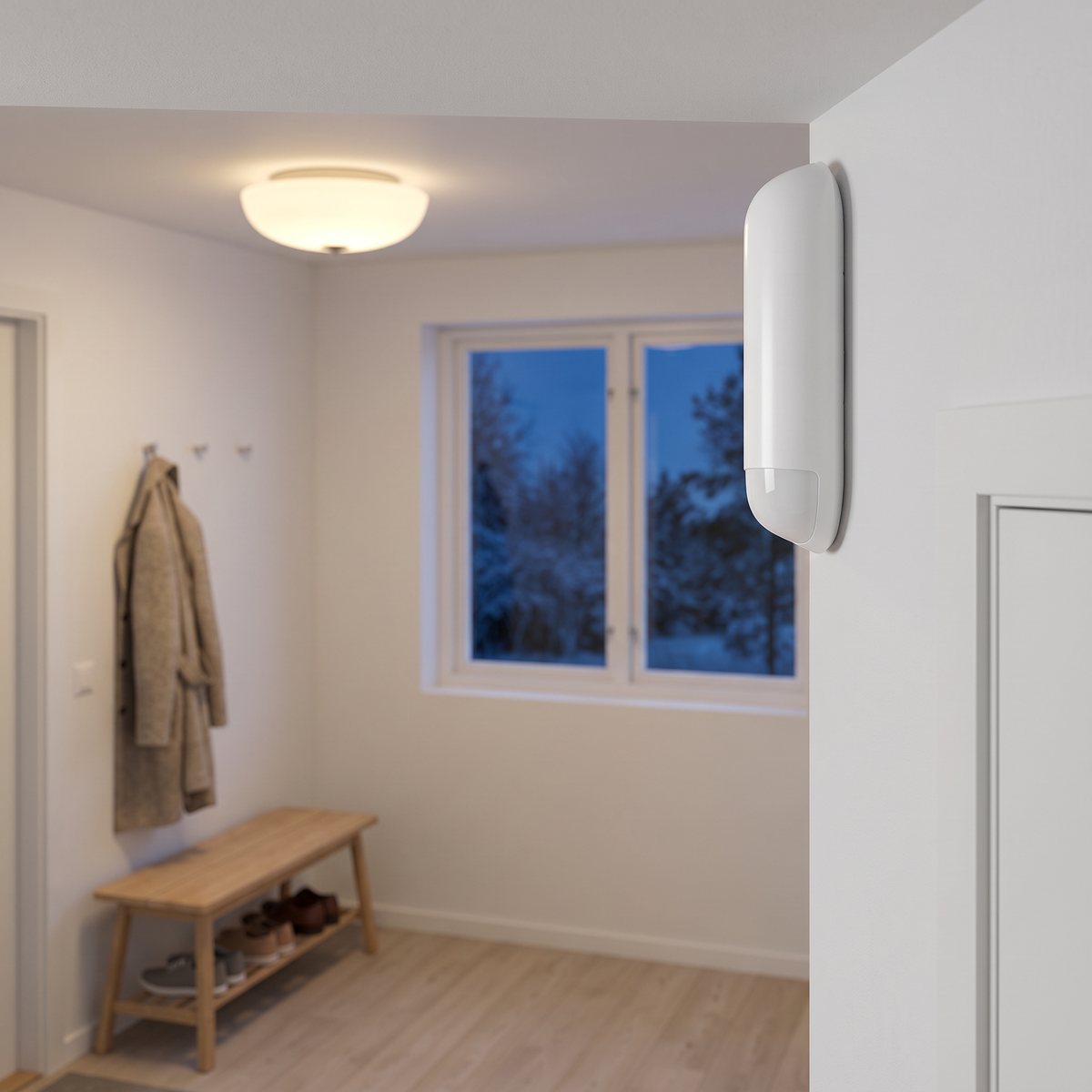 Smal vit Plejd WMS-01 rörelsesensor högt uppe vid väggen i en ljus hall med tänd taklampa, klädkrokar och skobänk