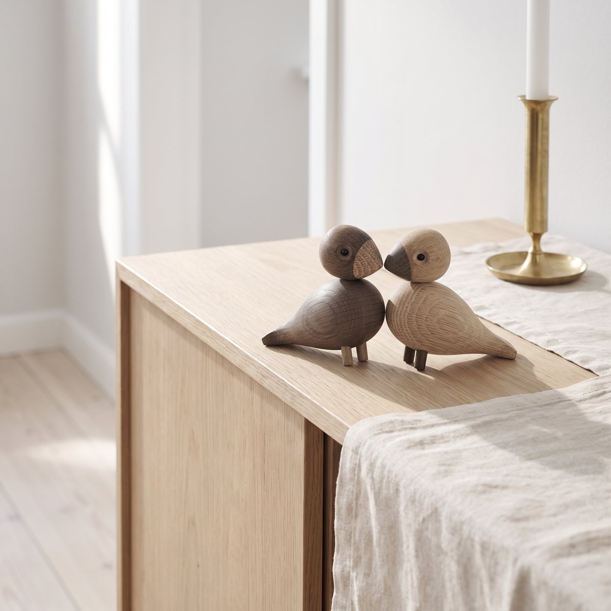 Kay Bojesens Turturduvor, en fågel i ljus ek och en i rökt ek, står näbb mot näbb på en sideboard med linneduk